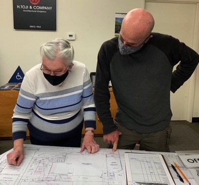 Photo of Sharon Toji and Chris Sircello reading a set of architectural floor plans.